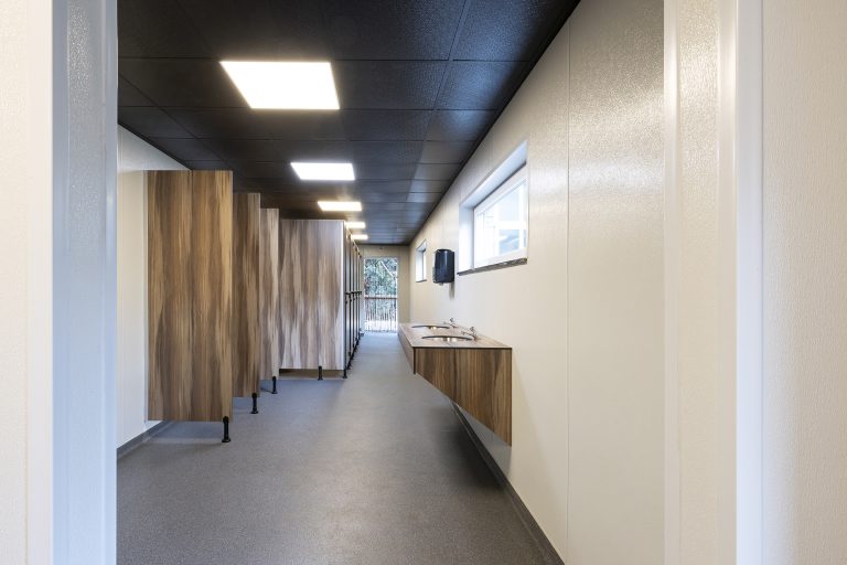 Gang met houtlook cabines en wastafels langs de raamzijde