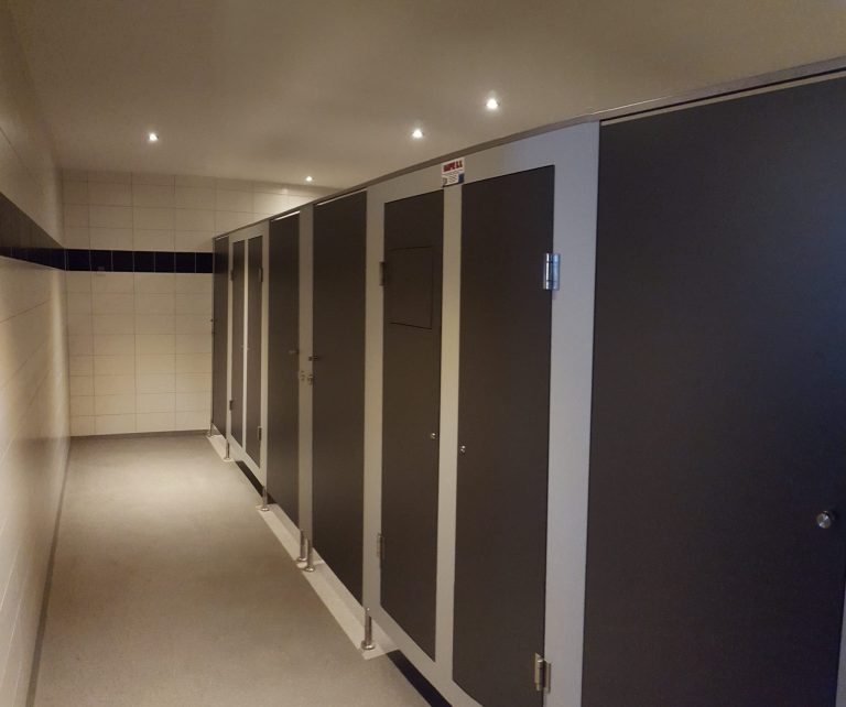 Lange gang met antracietkleurige deuren van een hygiënesluis langs een witte tegelwand