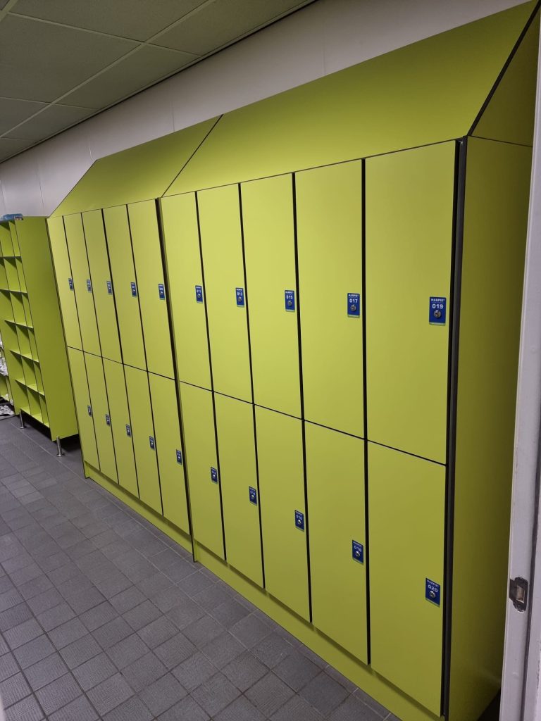 Limoengroene lockerwand met schuine kap in een gang met tegelvloer