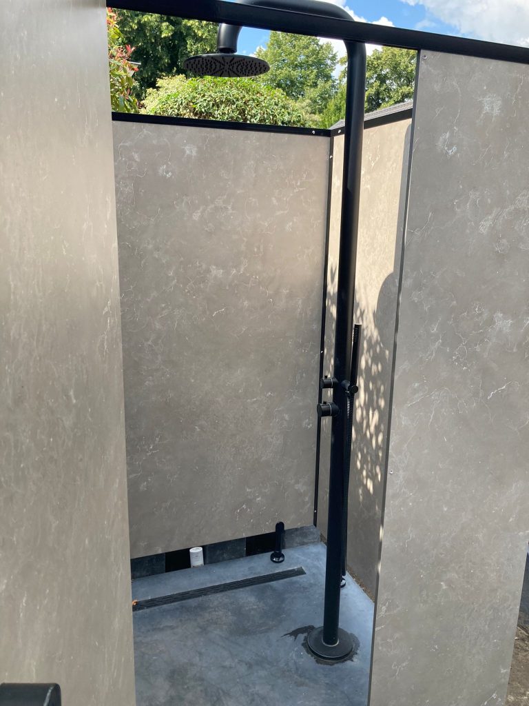 Open buitendouche met steenlook panelen en een zwarte douchestang