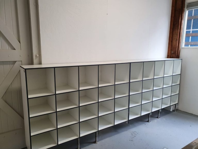 Lange witte schoenenkast met open vakken onder een raam