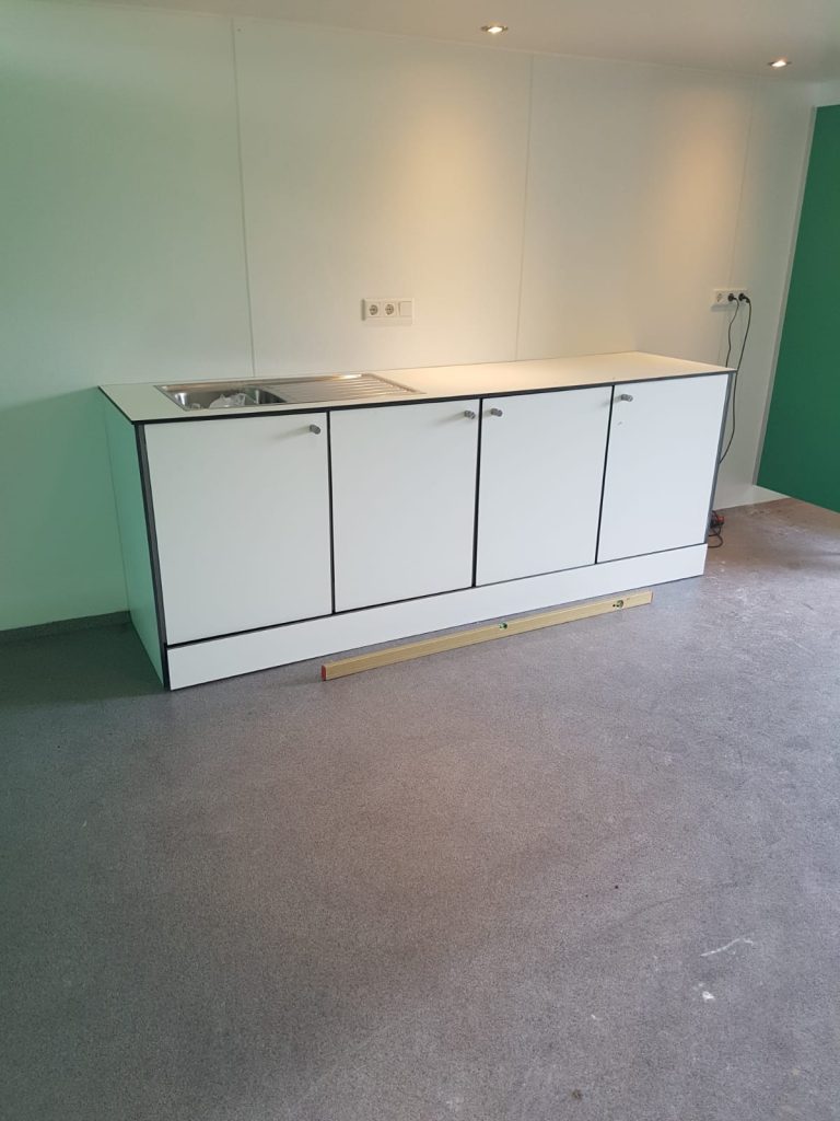 Wit keukenblok met vier deurtjes in een lege ruimte met groene wanden