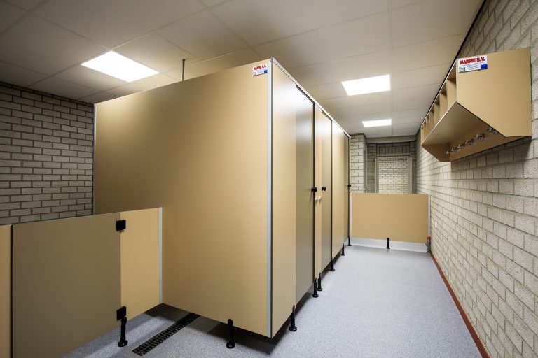 Gang in de hygiënesluis met beige cabines en een kapstokplank aan de wand